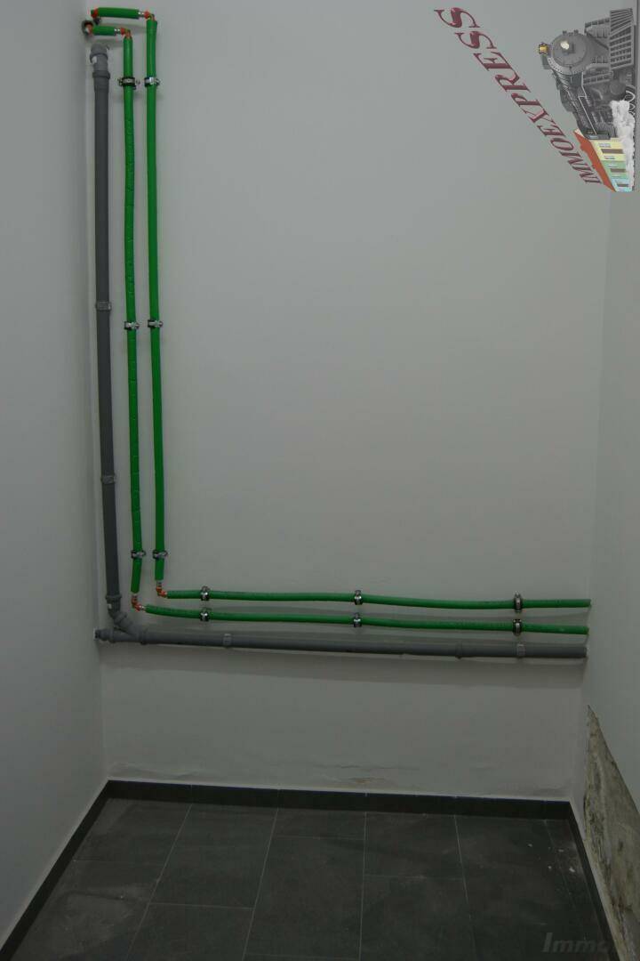 Versorgungsraum mit sichtbaren grünen und grauen Rohren an der Wand und Fliesenboden.