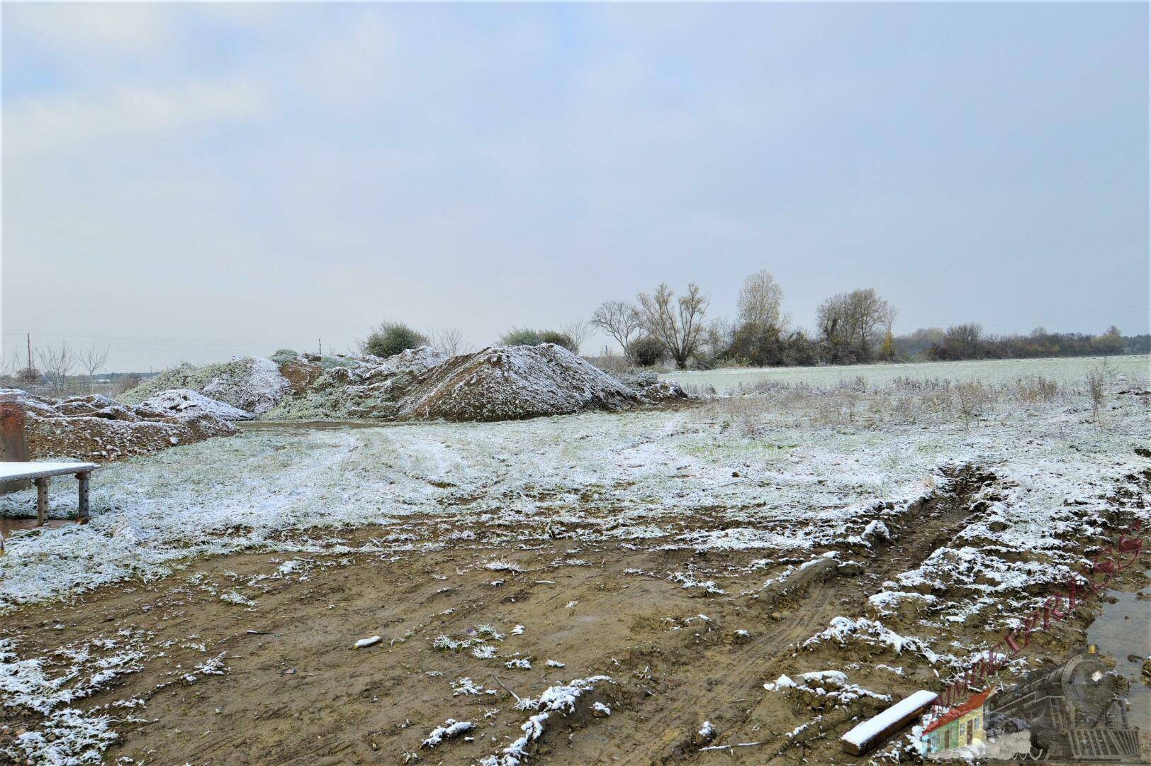 Offenes Grundstück mit Schneeresten und Erdhügeln, bereit für zukünftige Bebauung in ländlicher Umgebung.