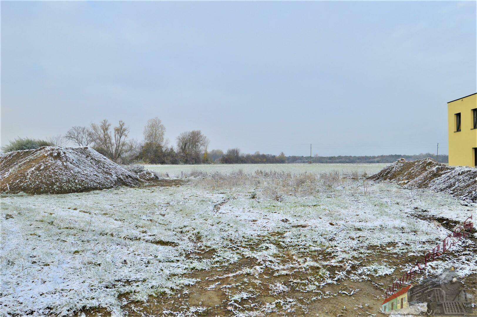 Weitläufiges unbebautes Grundstück mit leichter Schneedecke und Blick auf die offene Landschaft.