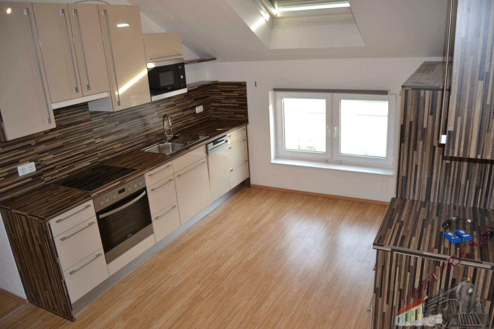 Dachgeschossküche mit Einbaugeräten, Holzarbeitsplatte und hellem Laminatboden.