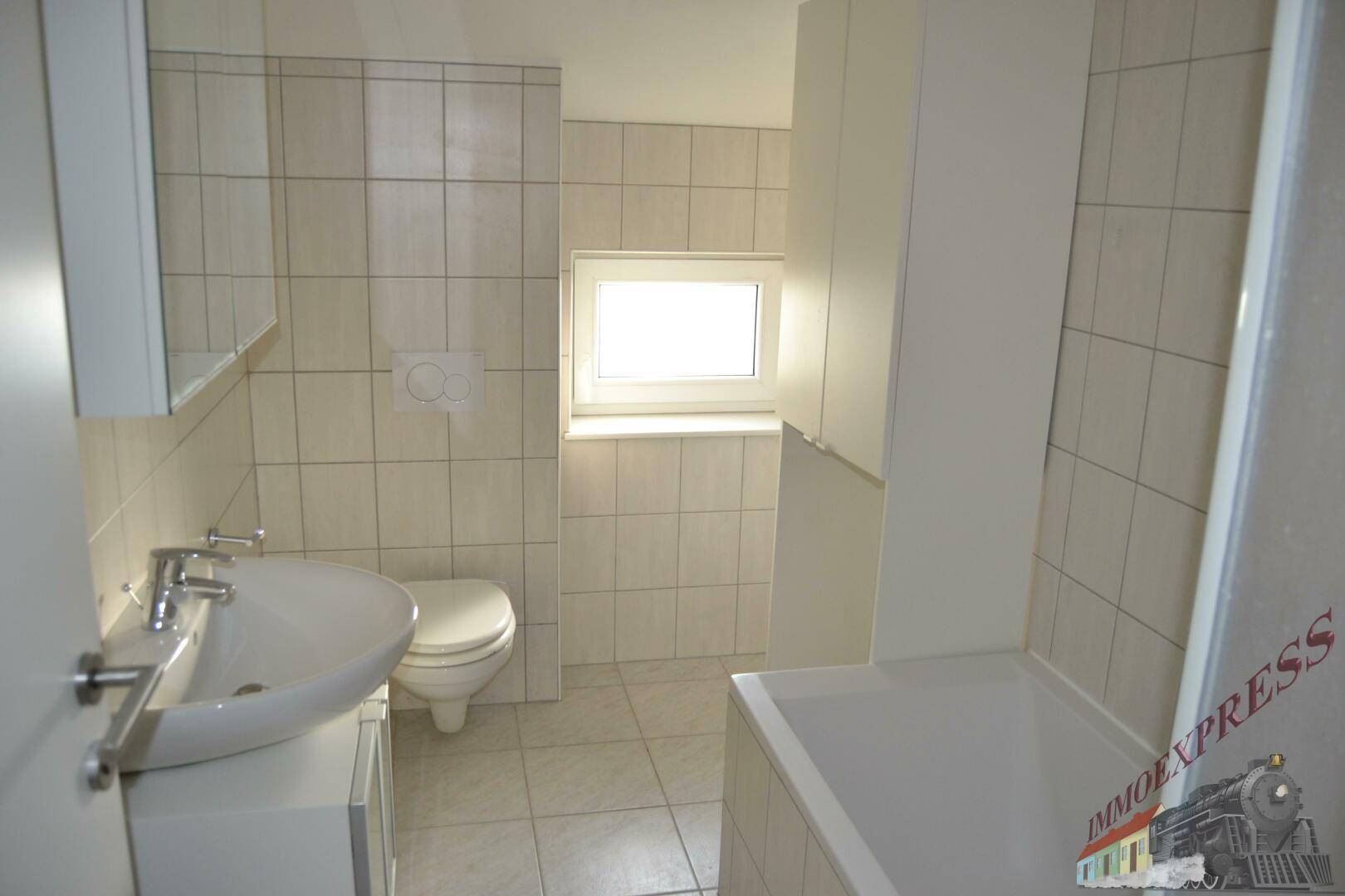 Helles Badezimmer mit Badewanne, WC und Fenster, komplett gefliest in neutralen Farben.