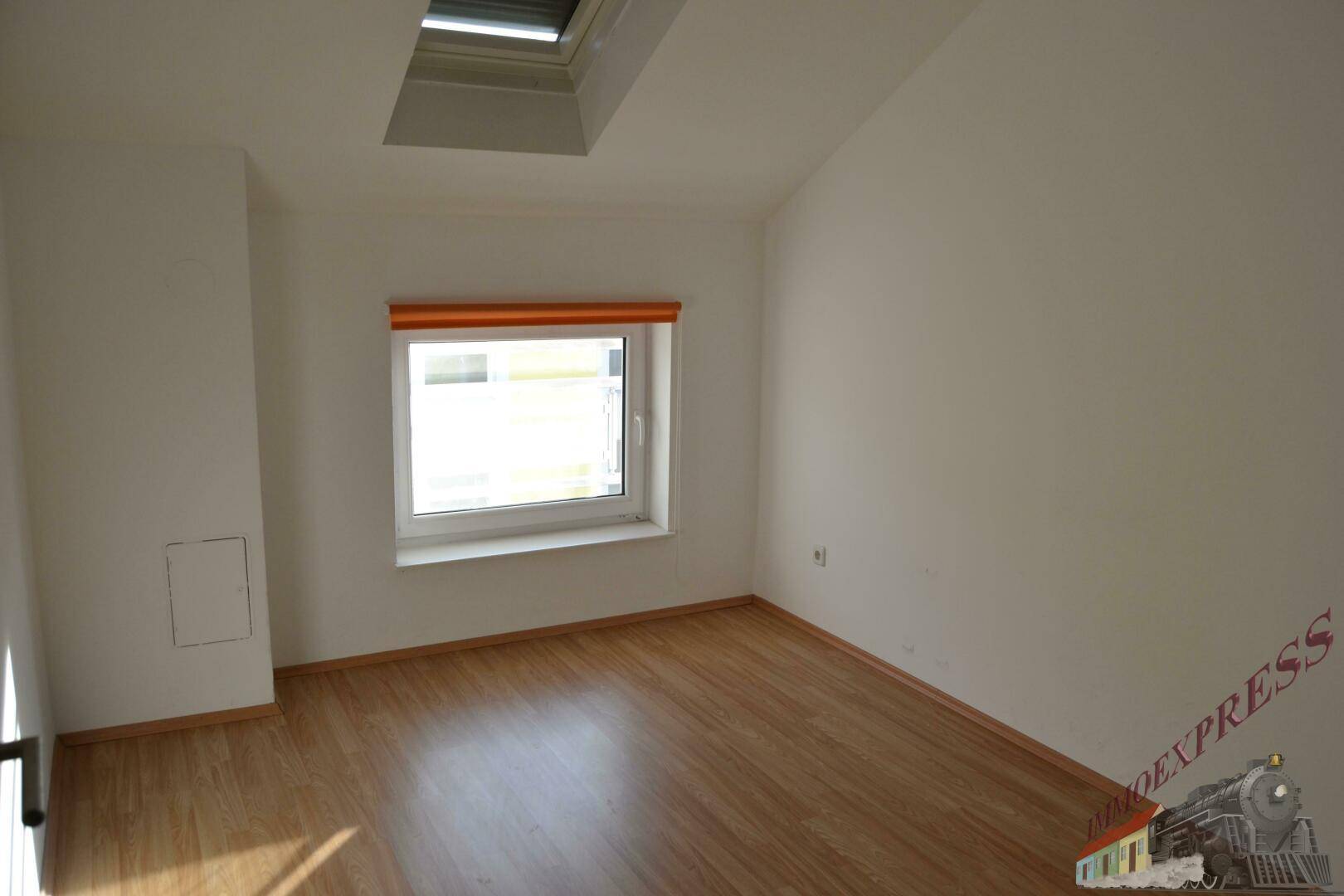 Leeres Zimmer im Dachgeschoss mit Laminatboden, Fenster und Dachfenster.
