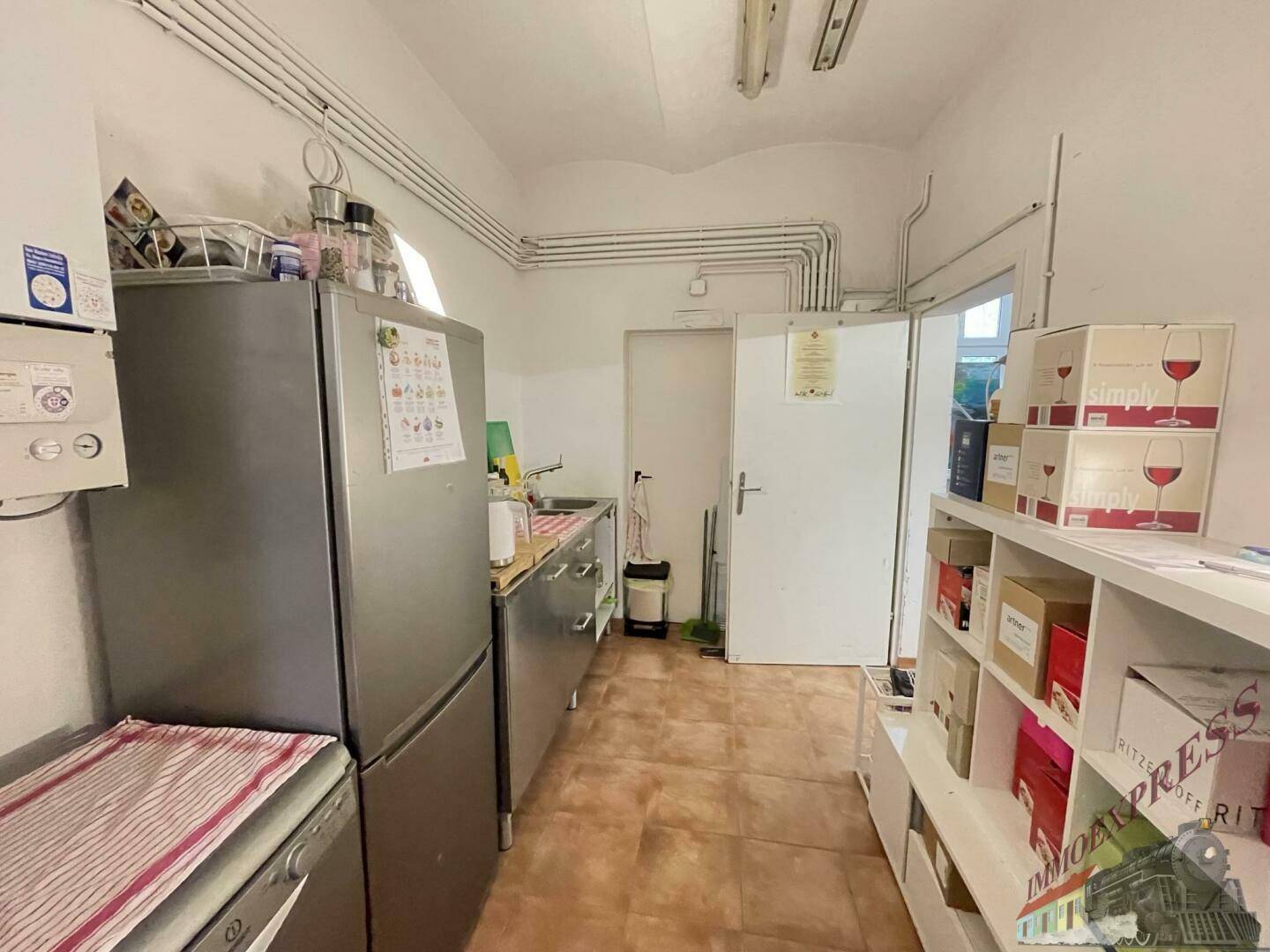Kleine Küchenzeile mit Kühlschrank, Spüle und Regalen, ideal für die Zubereitung von Speisen.