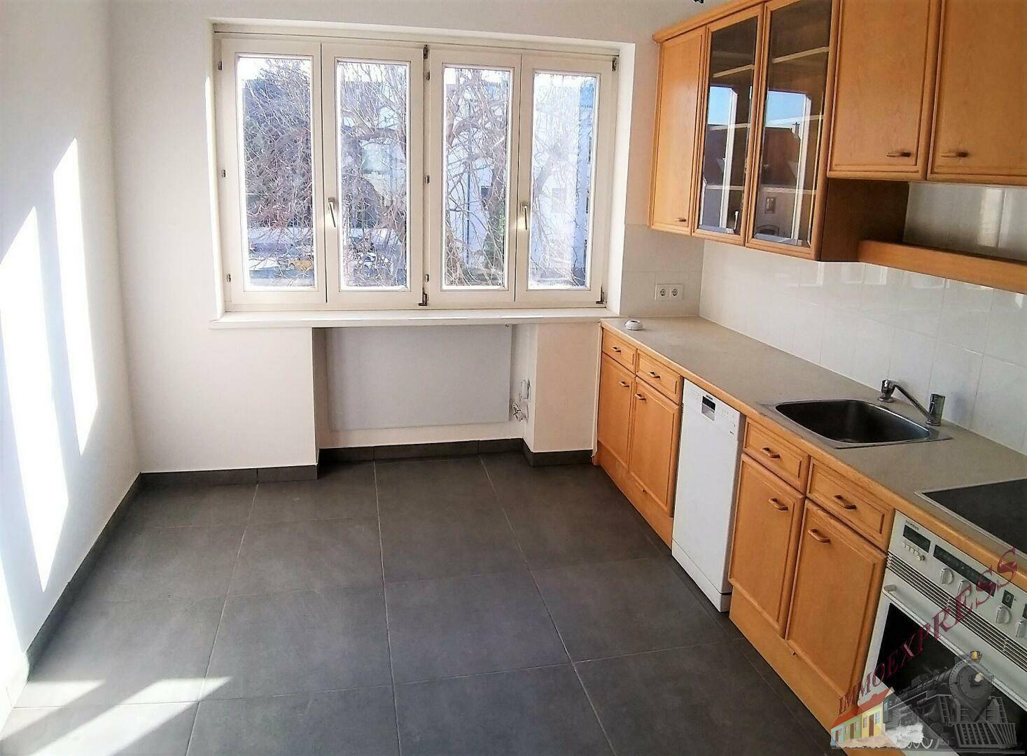 Küche mit Holzschränken, Fliesenboden, Fenster und integrierten Geräten.