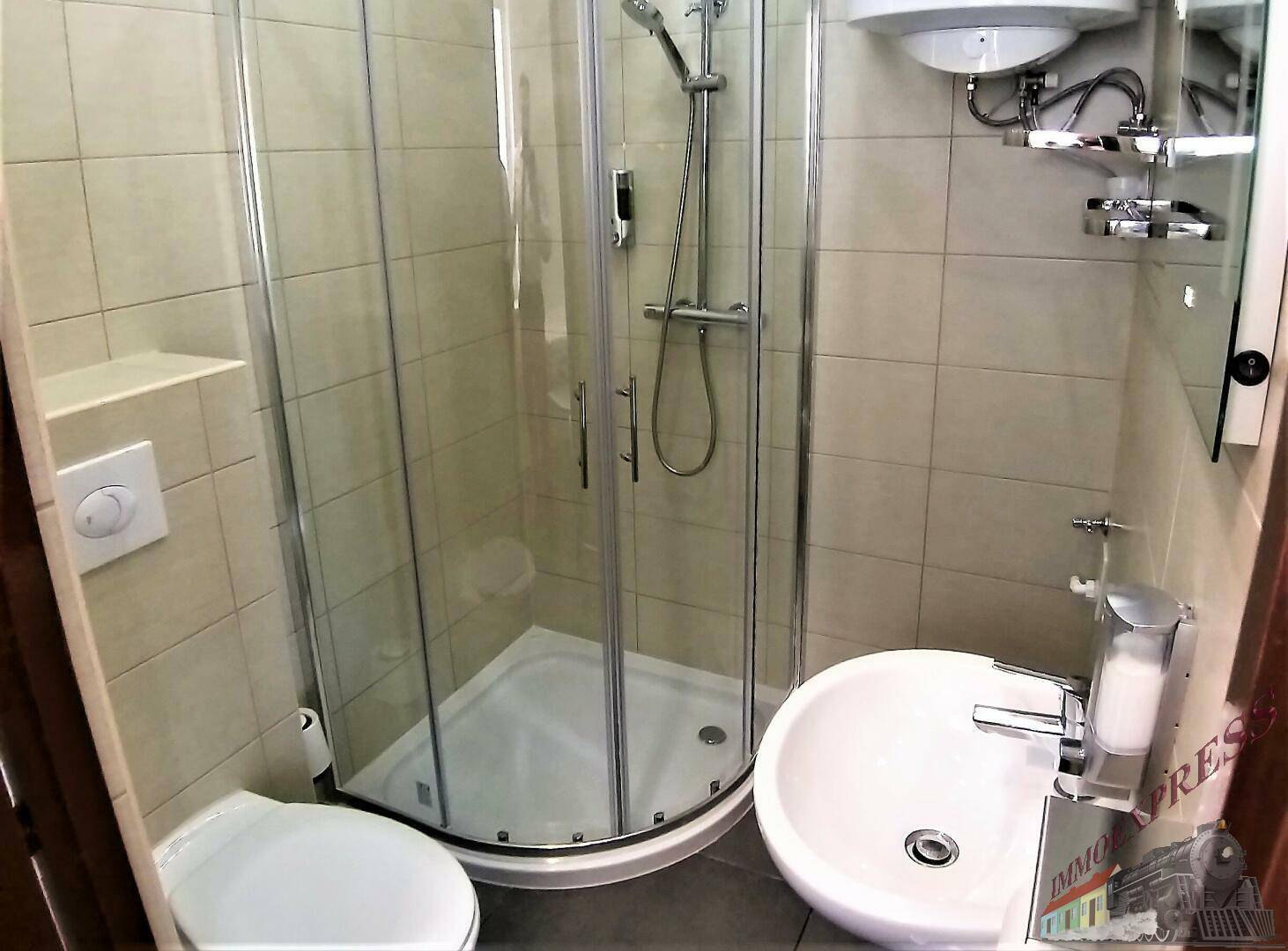 Modernes Badezimmer mit Eckduschkabine, Toilette und rundem Waschbecken auf beigefarbenen Fliesen.