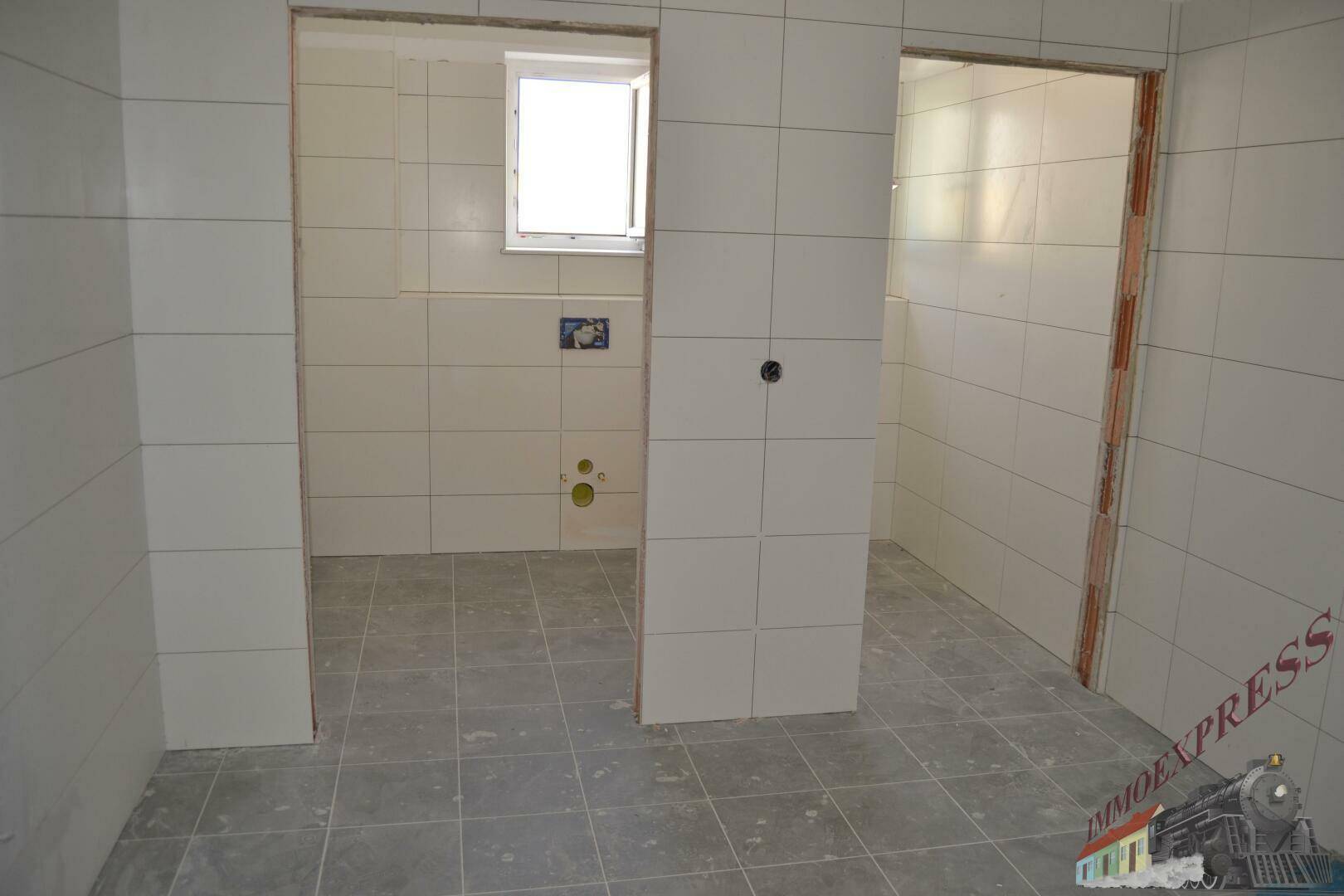 Badezimmer im Bau mit weißen Wandfliesen und grauen Bodenfliesen, vorbereitet für die Installation.