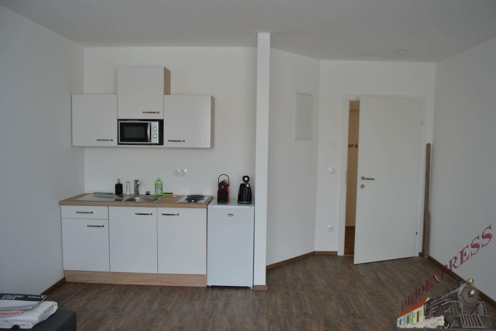Offenes Studio-Apartment mit kompakter Küchenzeile und Eingangstür, ideal für Einzelpersonen oder Paare.