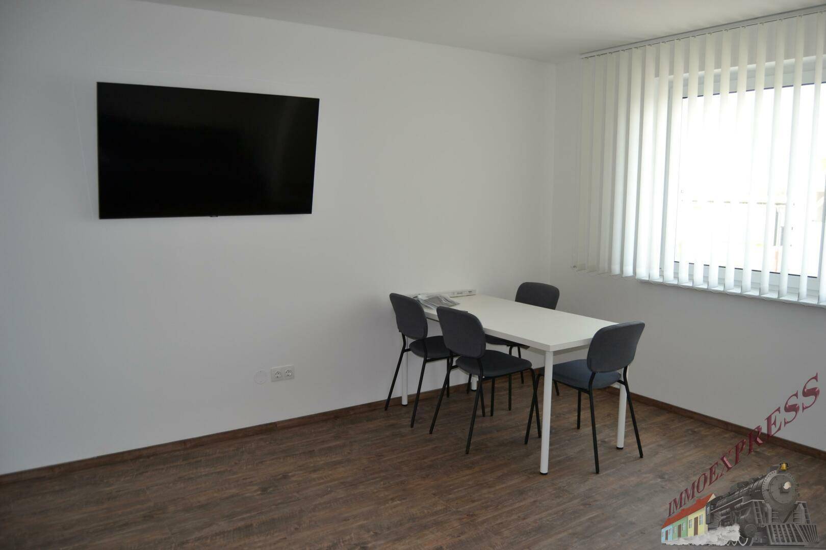 Heller Essbereich mit modernem Esstisch, vier Stühlen und einem an der Wand montierten Fernseher.