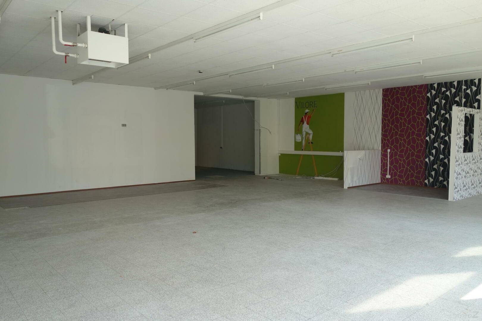 Großer, offener Verkaufsraum mit Fliesenboden und verschiedenen Wandgestaltungen, bereit für neue Mieter.