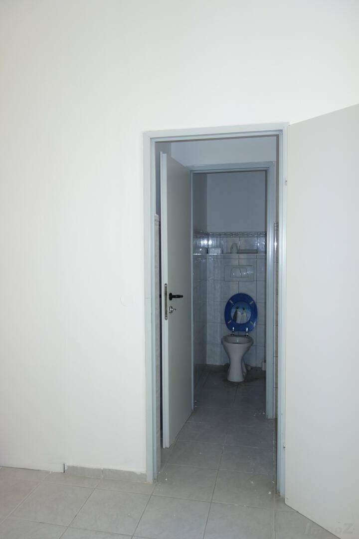 Einfache Toilette mit Fliesen an Wänden und Boden, ausgestattet mit einem WC und einem Fenster.