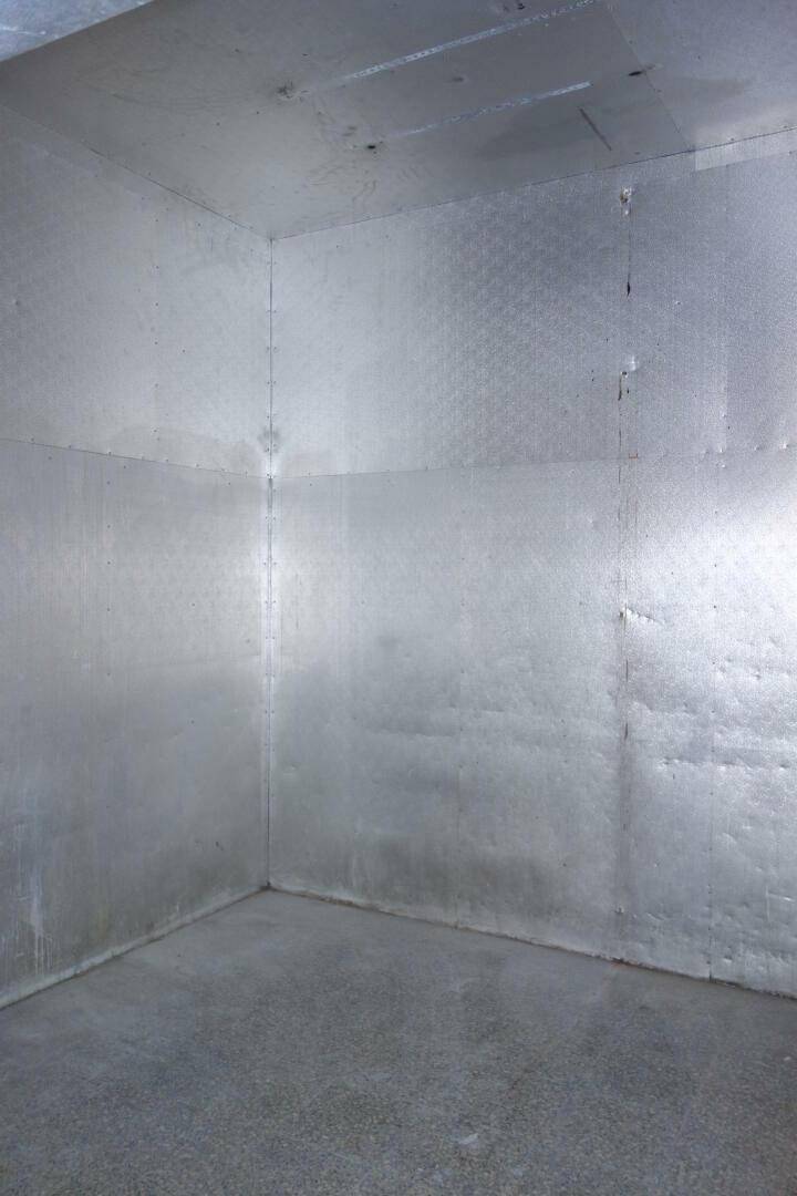Innenansicht eines Kühlraums mit metallverkleideten Wänden und Betonboden.