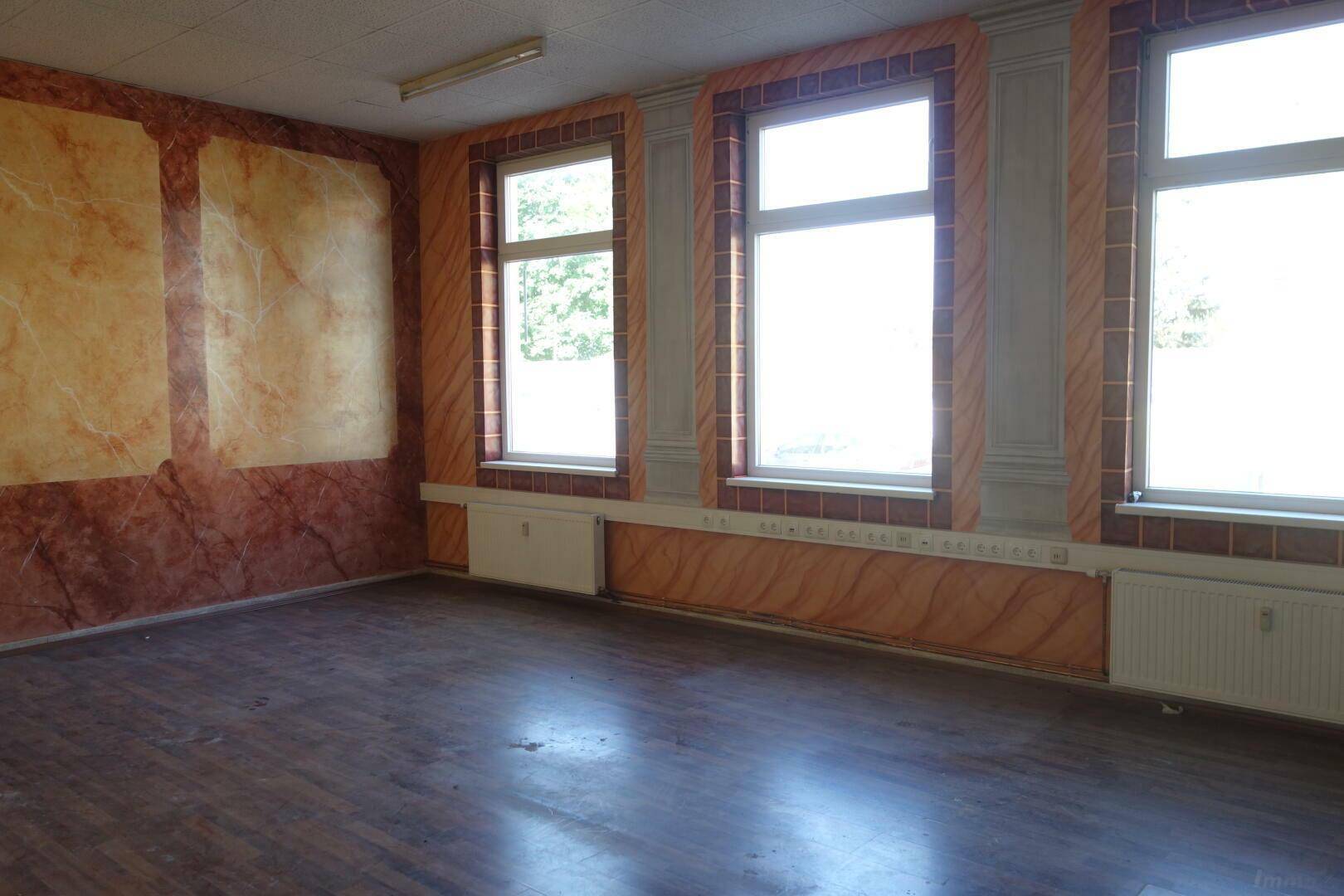 Raum mit dekorativen Wandpaneelen, Holzfußboden und Fenstern zur Außenseite.