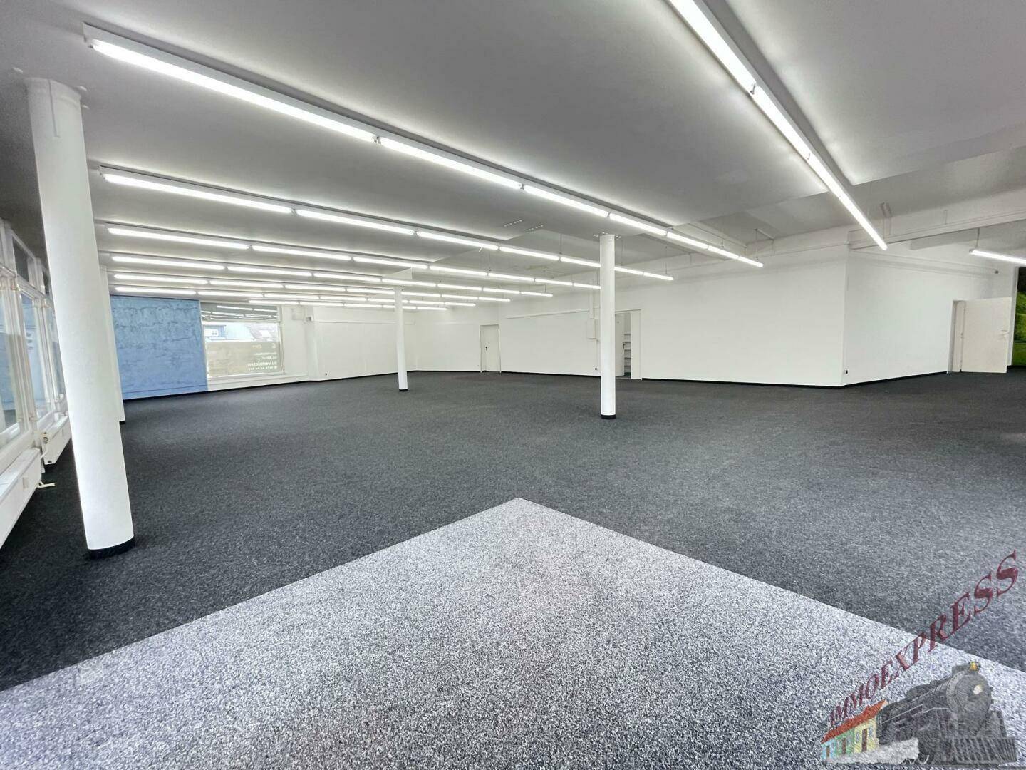 Geräumiger Verkaufsraum mit dunklem Teppichboden und weißen Säulen, bereit für die Einrichtung.