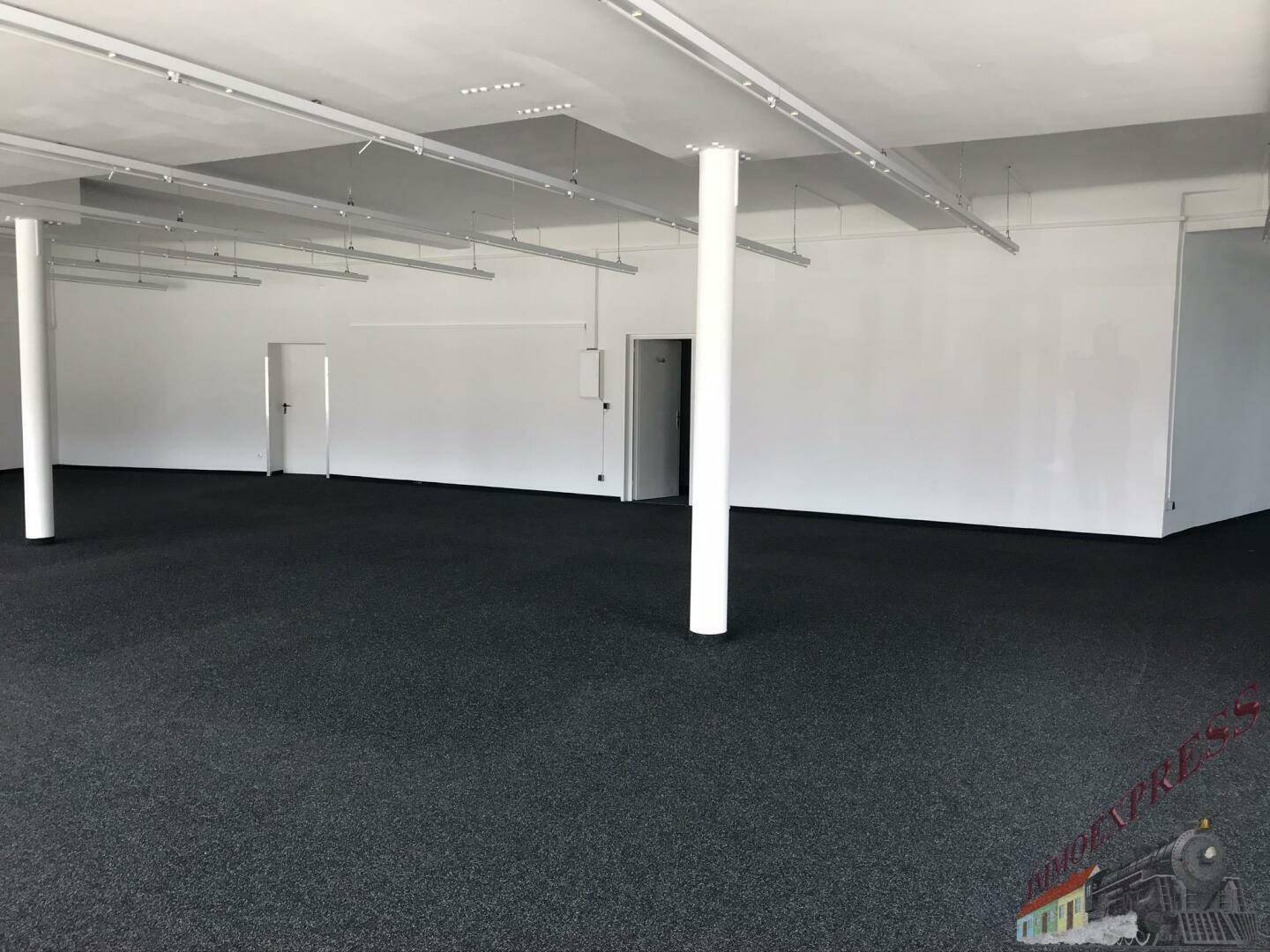 Großer, leerer Geschäftsraum mit Teppichboden, weißen Wänden und mehreren Säulen.