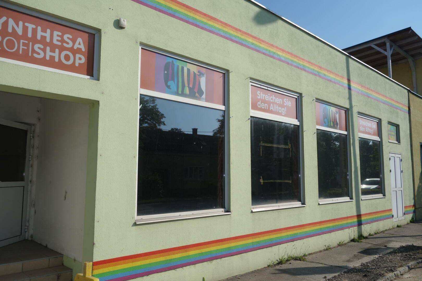 Buntes Geschäftsgebäude mit Regenbogenstreifen und großen Schaufenstern, das eine lebendige Atmosphäre schafft.