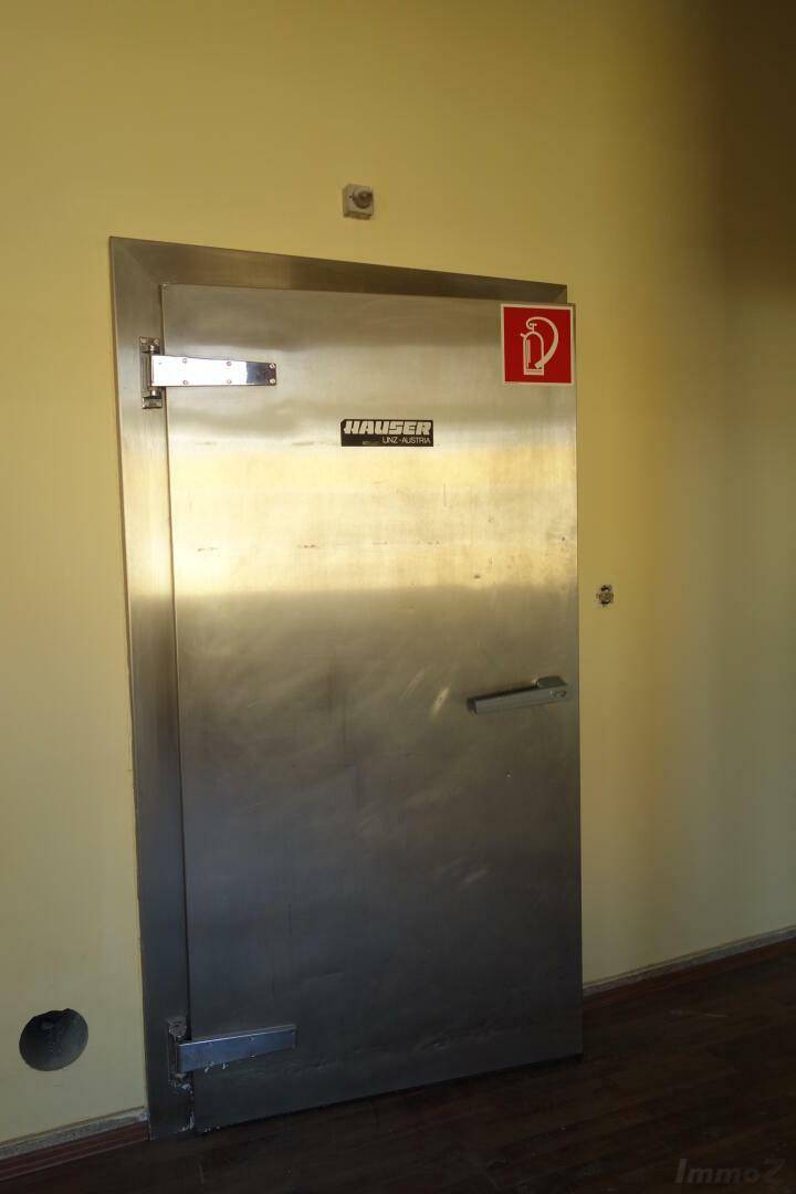 Robuste Metalltür mit Brandschutzzeichen in einem Raum, der als Lager oder Kühlraum dienen könnte.