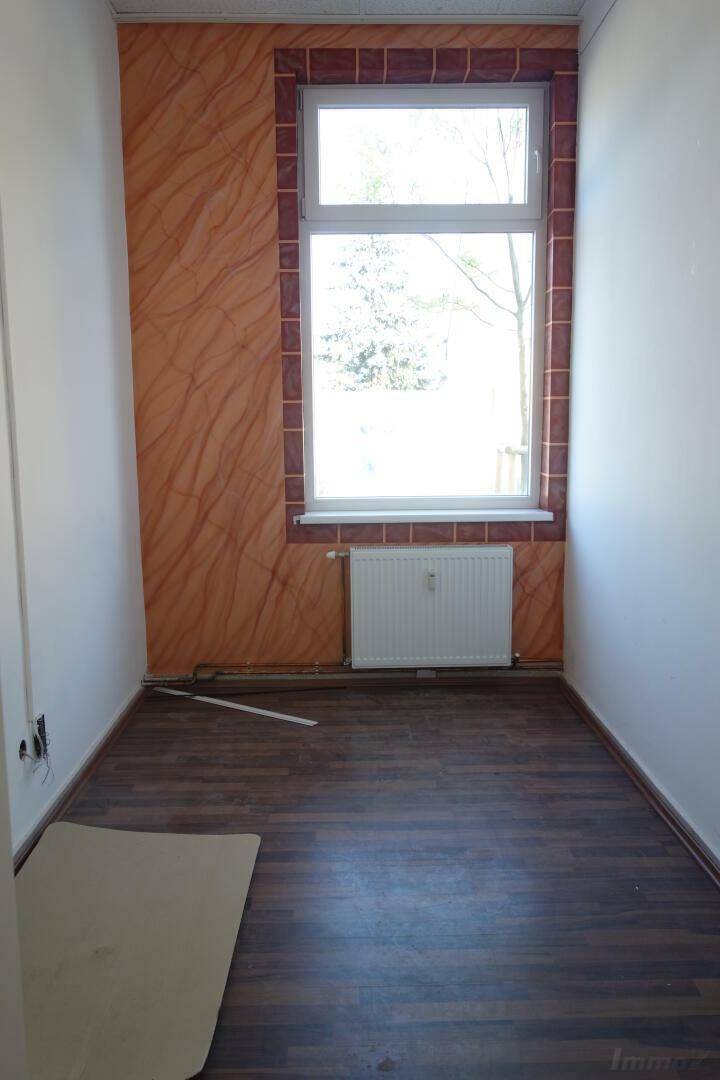 Kleiner Raum mit Holzboden und dekorativen Wandpaneelen, ausgestattet mit einem Heizkörper unter dem Fenster.