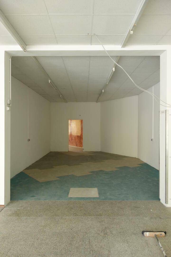 Großer, leerer Gewerberaum mit abgehängter Decke und unterschiedlichen Bodenbelägen, der Renovierung benötigt.