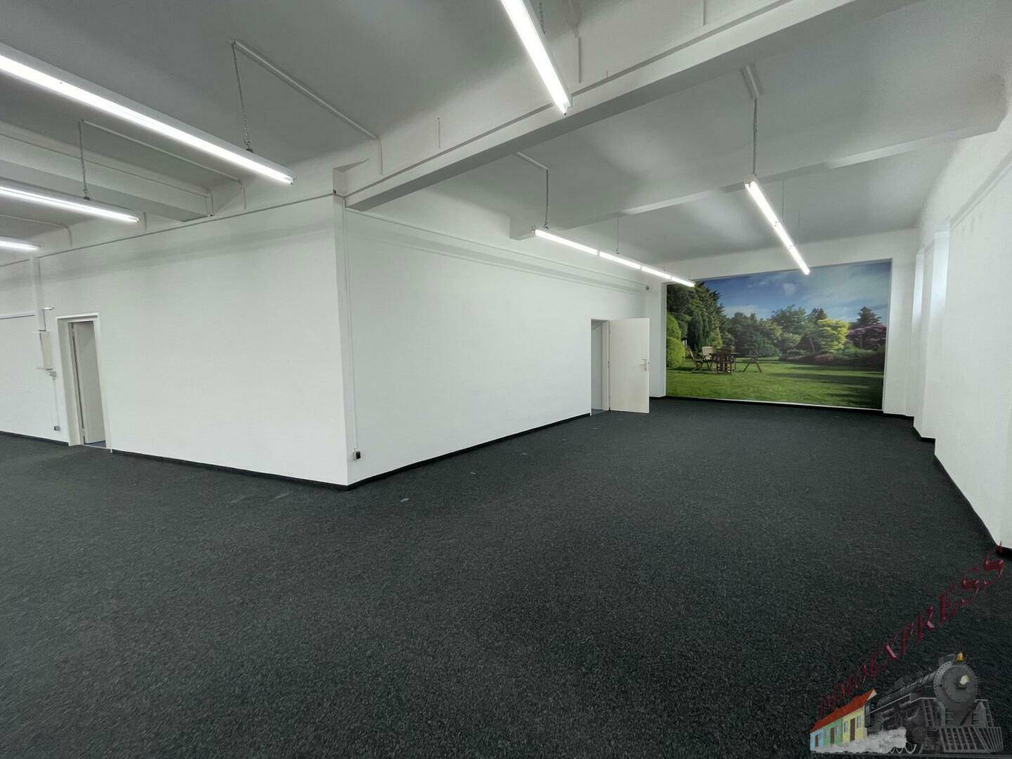 Heller Verkaufsraum mit Teppichboden und einer großen Wandtapete, die eine grüne Landschaft darstellt.