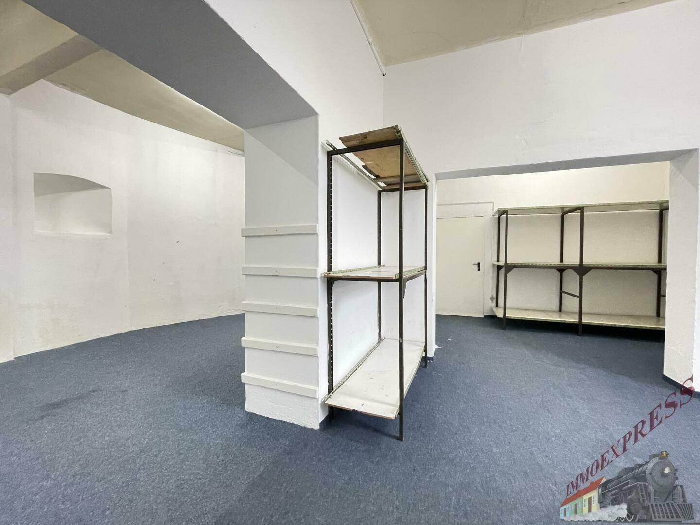 Kellerraum mit blauem Teppichboden und einfachen Regalen, ideal als Lagerfläche nutzbar.