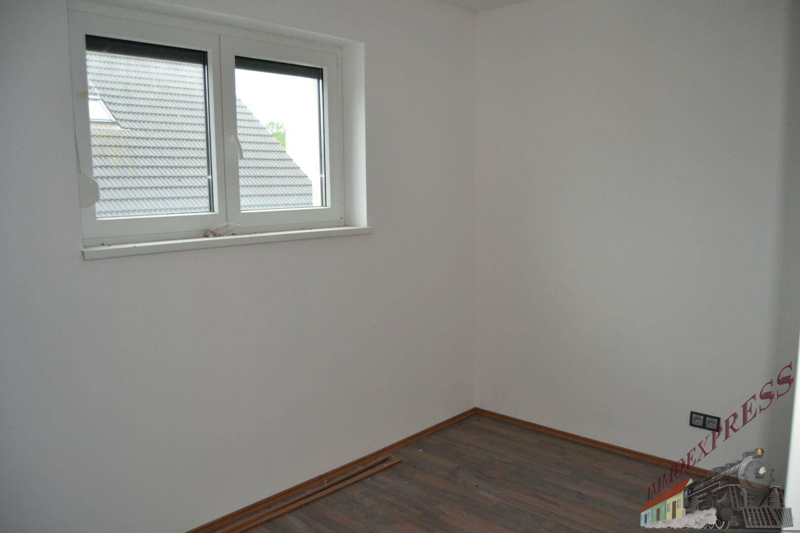 Helles Zimmer mit Laminatboden und Fenster, das einen Blick auf das Dach bietet.