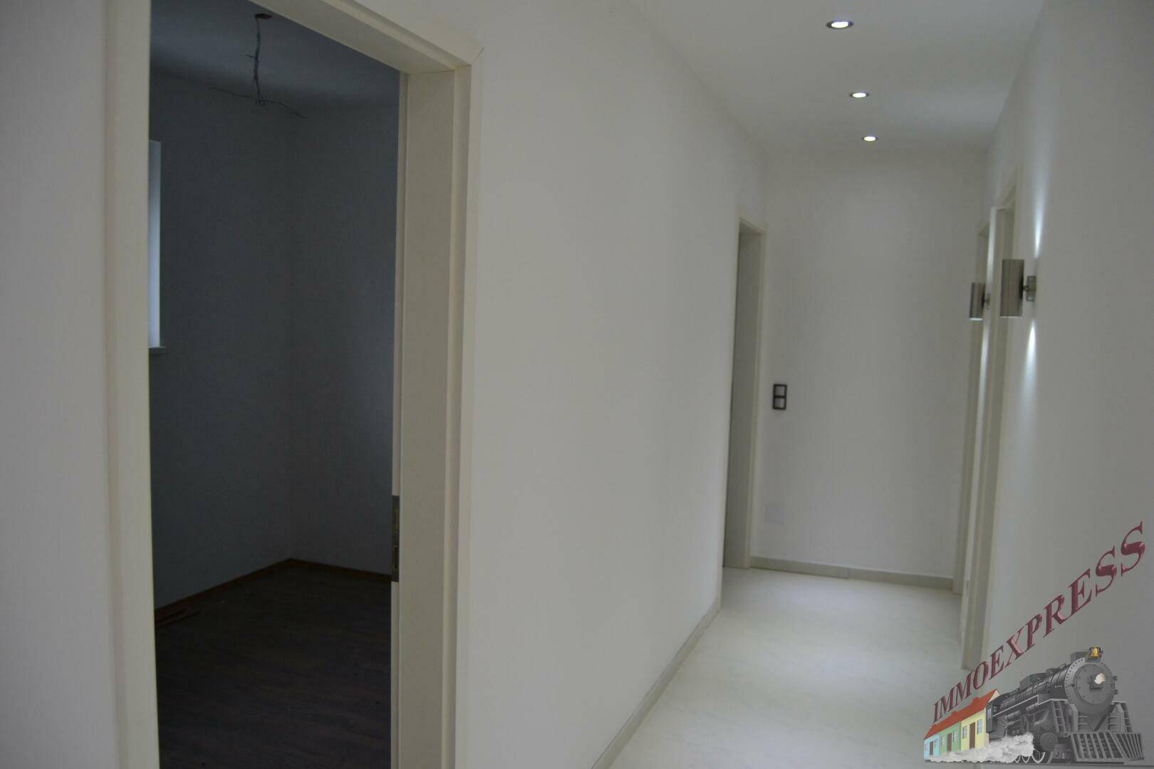 Heller Flur mit weiß gestrichenen Wänden und Einbaustrahlern, der zu den Zimmern führt.