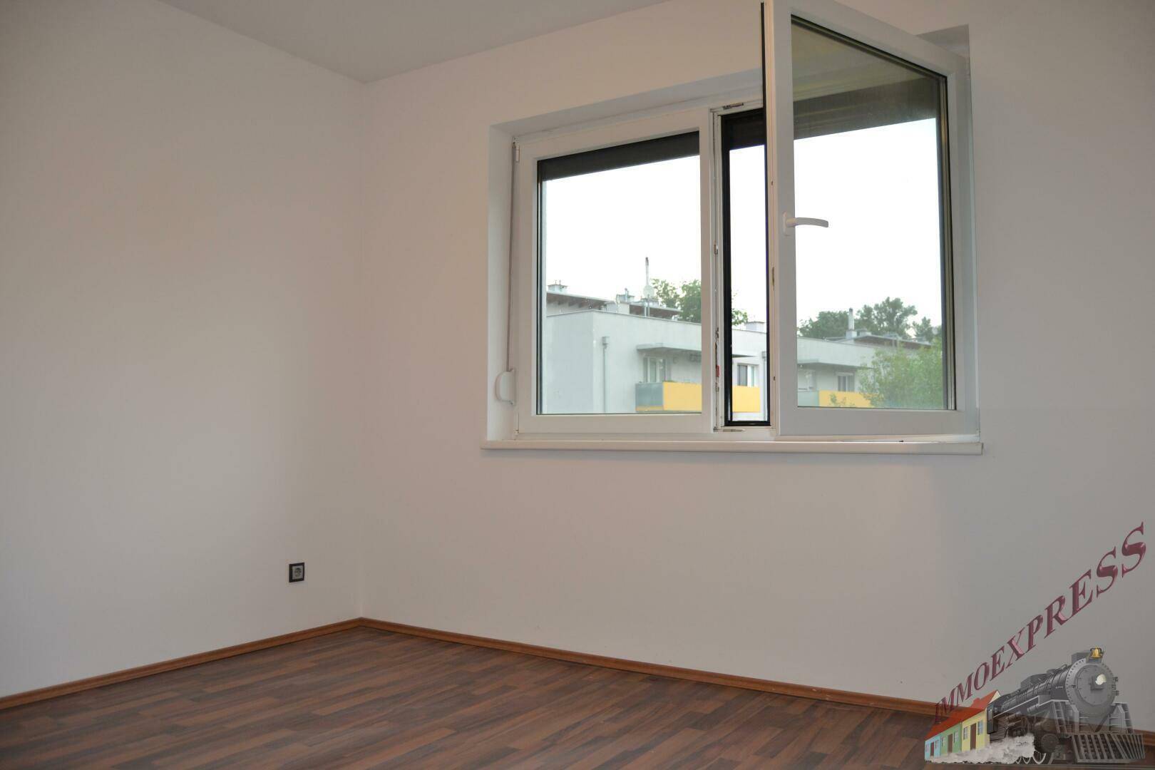 Helles Zimmer mit Laminatboden und großem Fenster, das viel Tageslicht hereinlässt.
