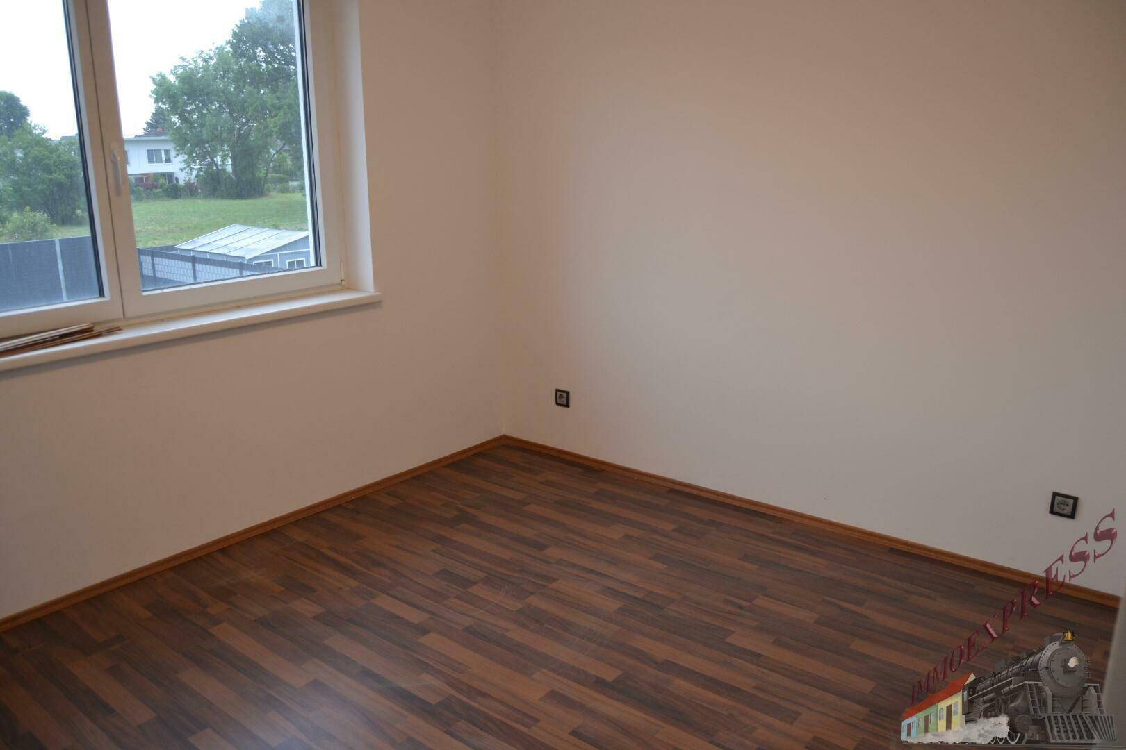 Helles Zimmer mit Laminatboden und Fenster, das einen Blick ins Grüne bietet.