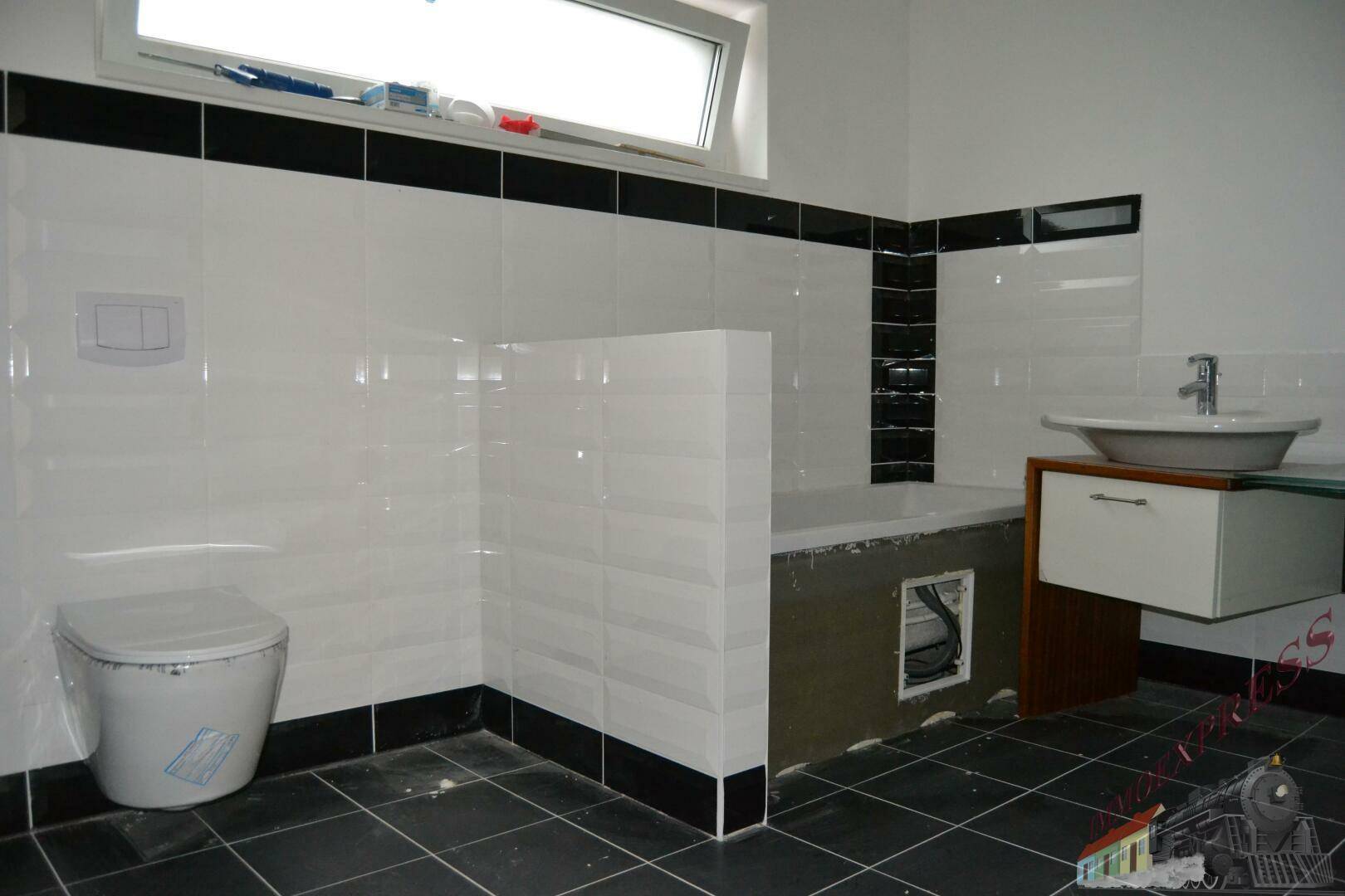 Modernes Badezimmer in Schwarz-Weiß-Fliesen mit WC, Waschbecken und vorbereiteter Badewanne.