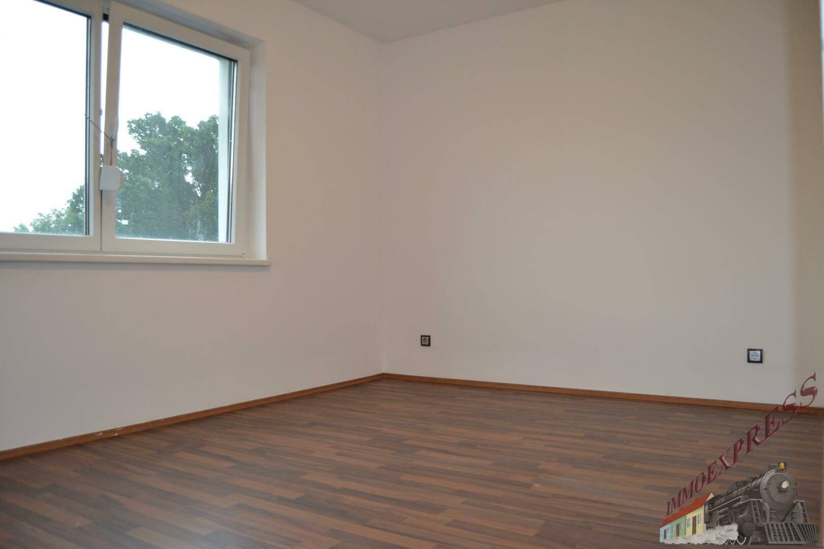 Helles Zimmer mit Laminatboden und Fenster, das einen weiten Blick ins Grüne ermöglicht.