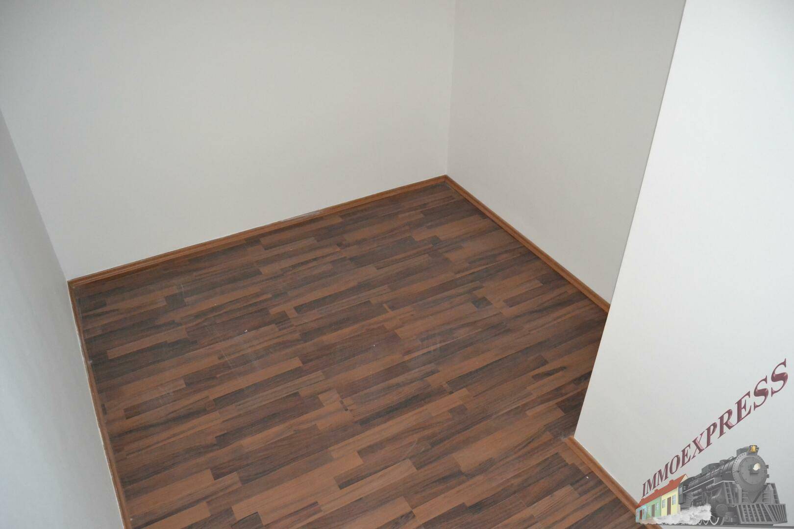 Leeres Zimmer mit dunklem Laminatboden und weißen Wänden, bereit zur individuellen Gestaltung.