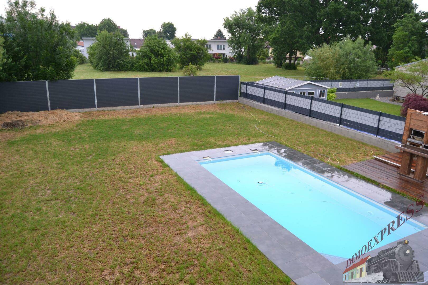 Weitläufiger Gartenbereich mit eingelassenem Pool, Rasenfläche und umzäuntem Grundstück.