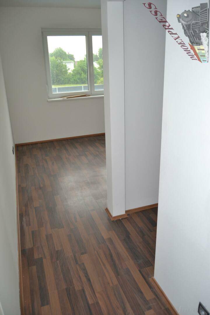 Leeres Zimmer mit Laminatboden und Fenster, das viel Tageslicht in den Raum bringt.
