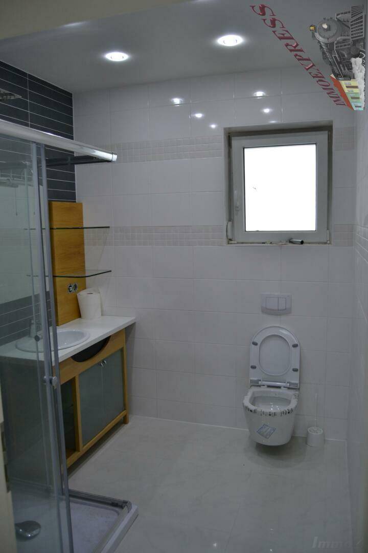 Modernes Badezimmer mit Duschkabine, WC, Waschbecken und Fenster für Tageslicht.