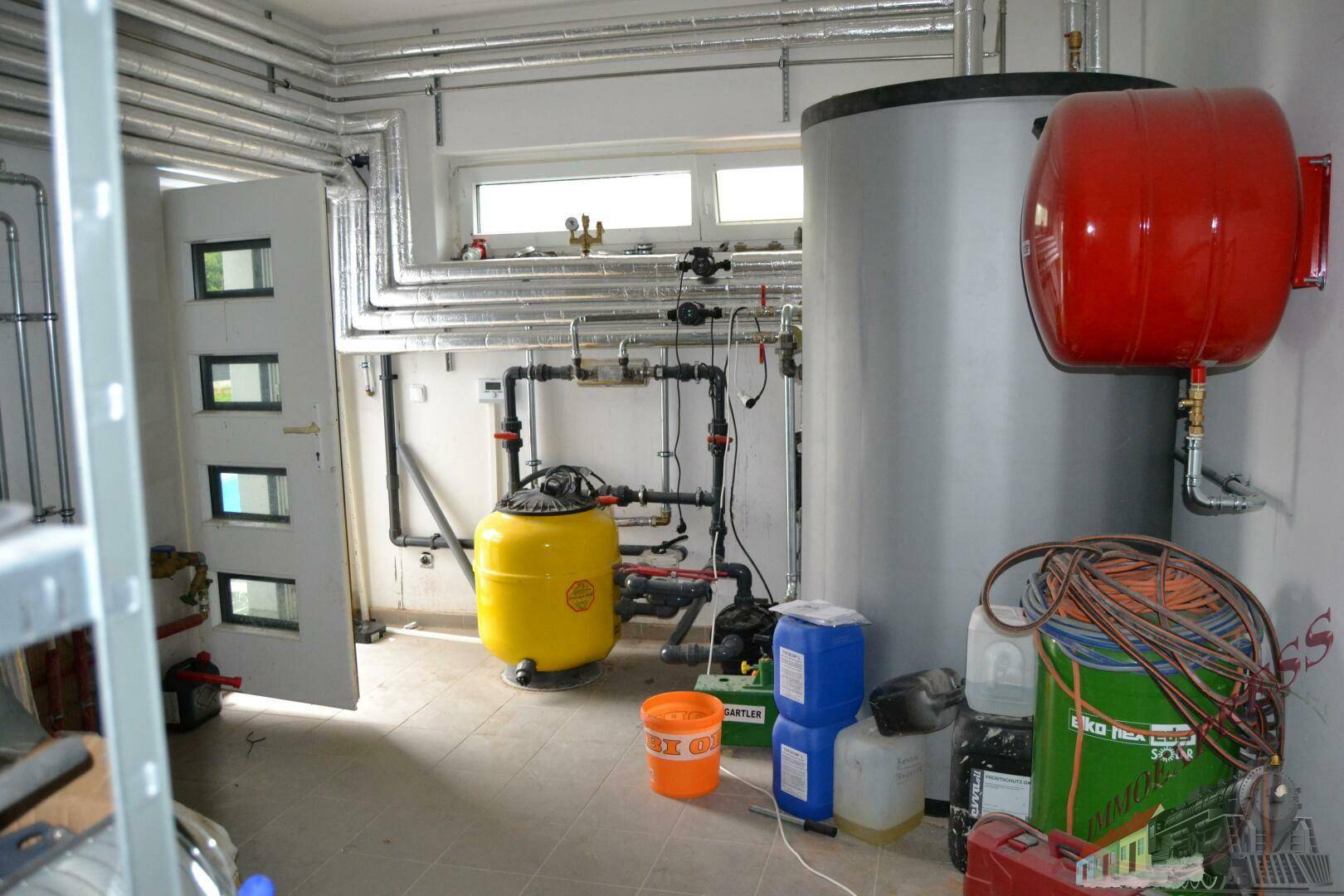 Heizungsraum mit Kesseln, Rohren und Fenstern für Belüftung.