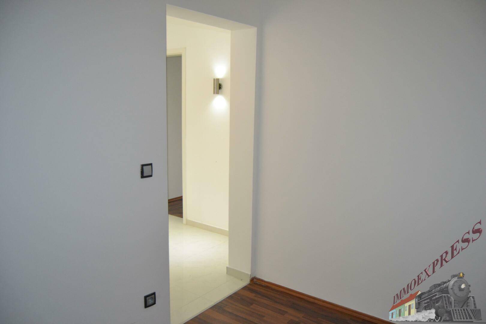 Heller Flur mit weiß gestrichenen Wänden, der zu einem weiteren Zimmer führt.