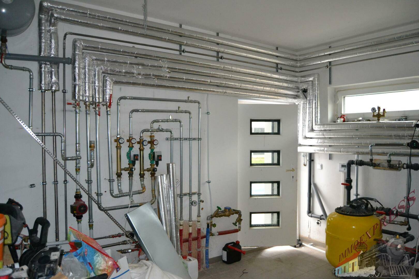 Technikraum mit umfangreicher Rohrinstallation, Heizungsanlage und Warmwasserspeicher.