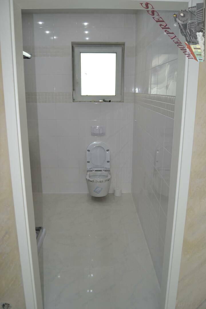 Helles WC mit wandhängender Toilette, Fenster und weißen Fliesen.