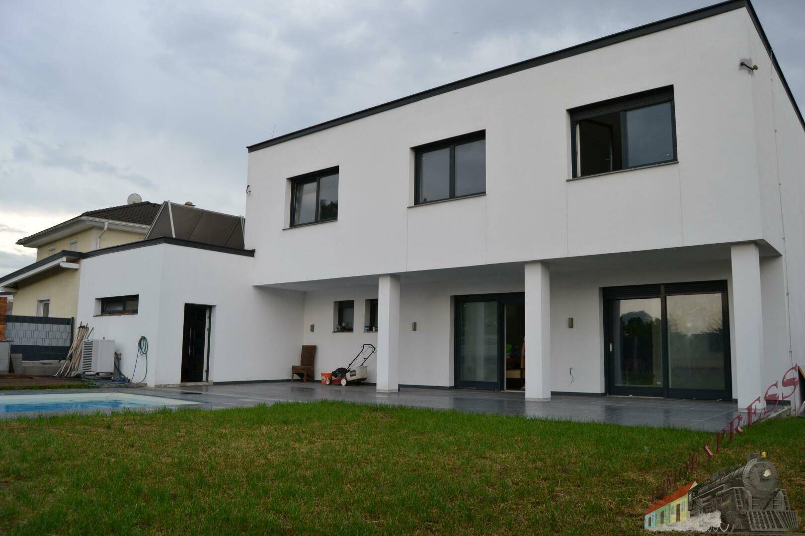 Moderne Hausfassade mit großzügiger Terrasse, Pool und Rasenfläche im Gartenbereich.