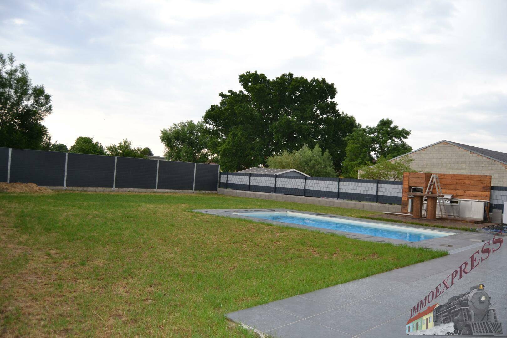 Weitläufiger Garten mit Rasenfläche, Pool und einer Outdoor-Küche, umgeben von einem modernen Zaun.