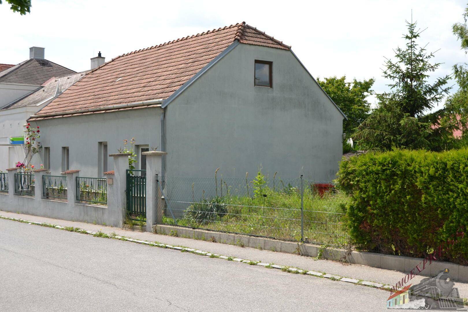 Seitenansicht des Hauses mit Ziegeldach, Hecke und einem kleinen Fenster im Dachgeschoss.