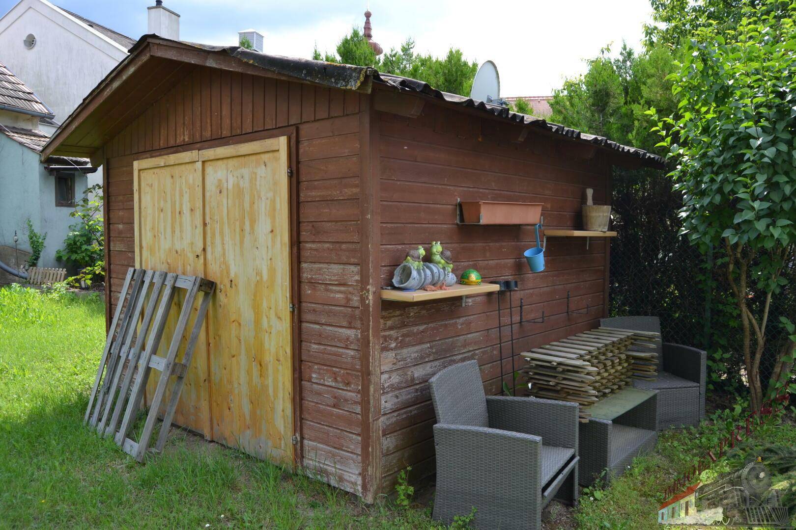 Rustikaler Holzschuppen im Garten mit Regalen und Gartenutensilien an der Außenwand.
