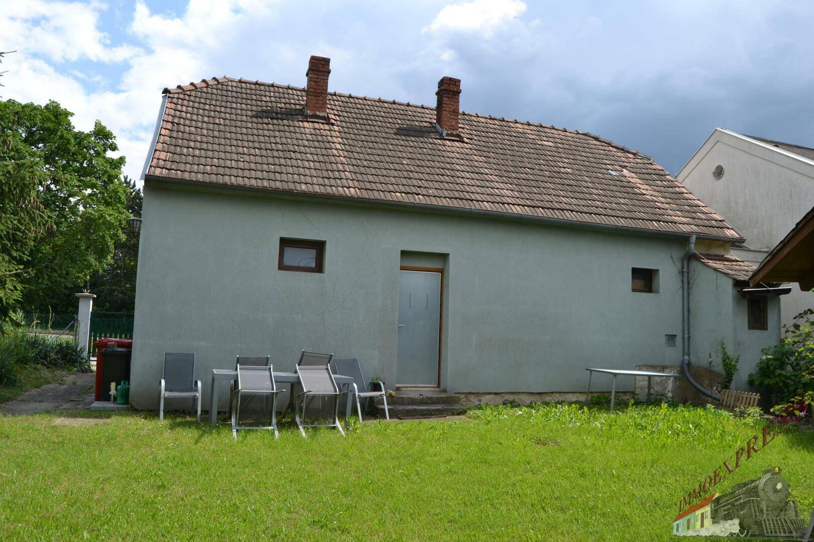 Hinterer Gartenbereich mit Rasenfläche, Außentür und einer Sitzecke am Haus.