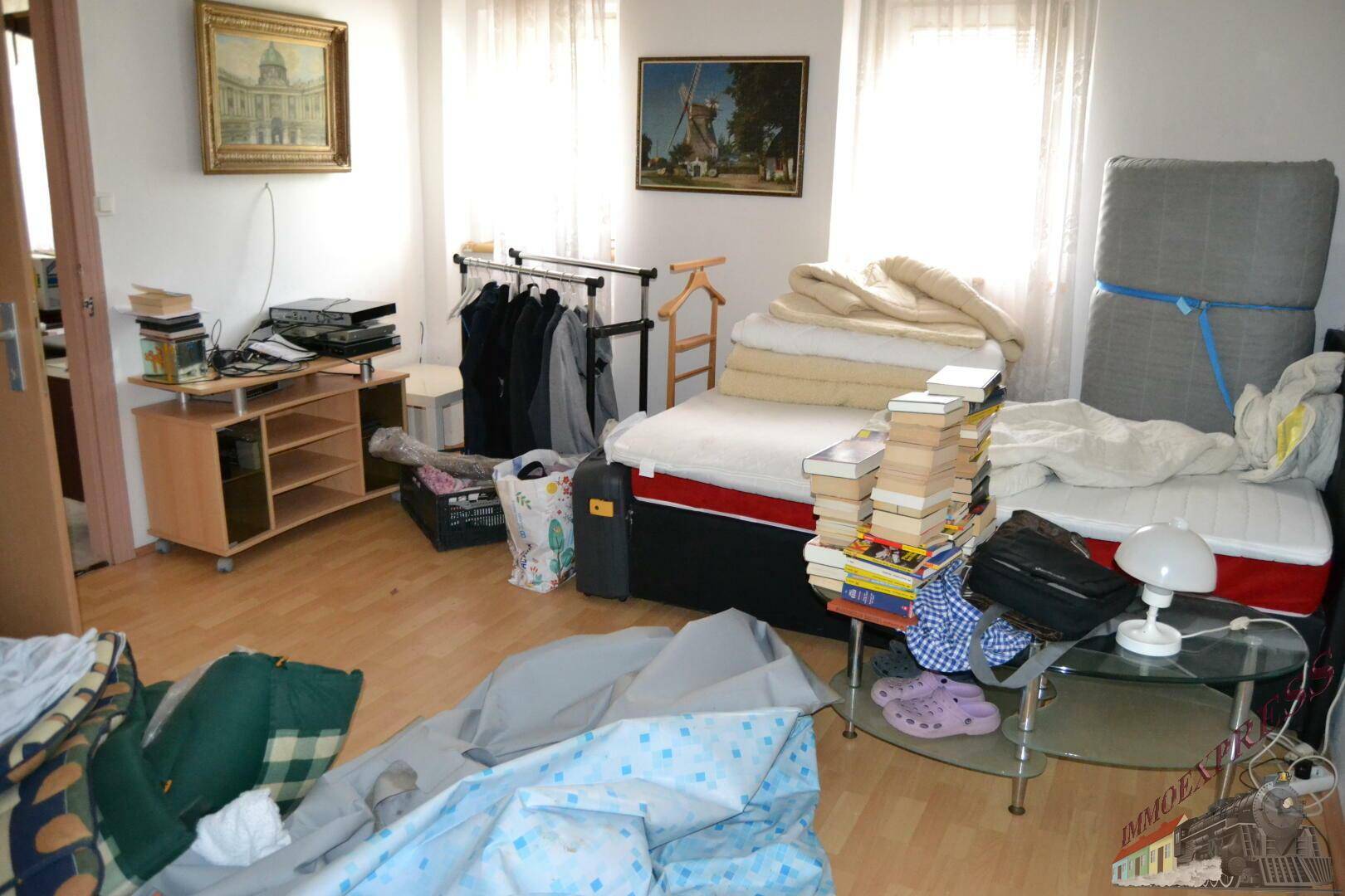 Helles Schlafzimmer mit Parkettboden, einem Bett und verschiedenen persönlichen Gegenständen.