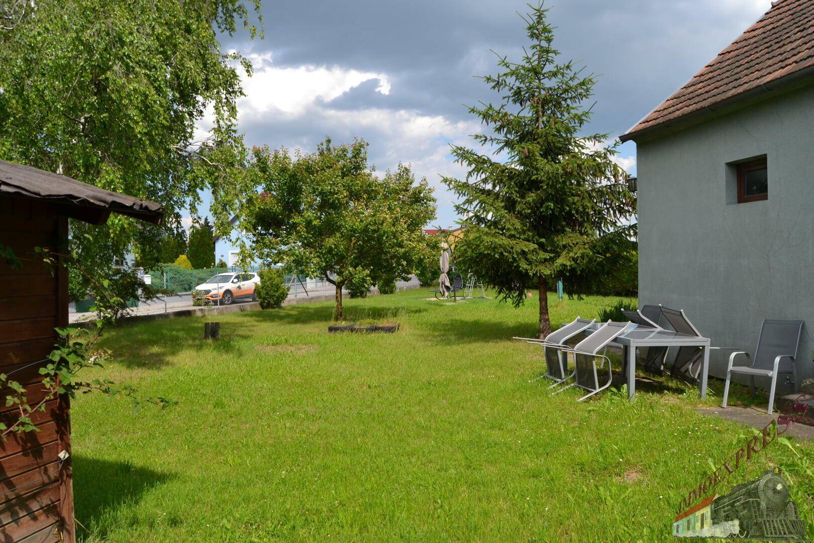 Gartenbereich mit Rasenfläche, Bäumen und einer kleinen Sitzecke neben dem Haus.