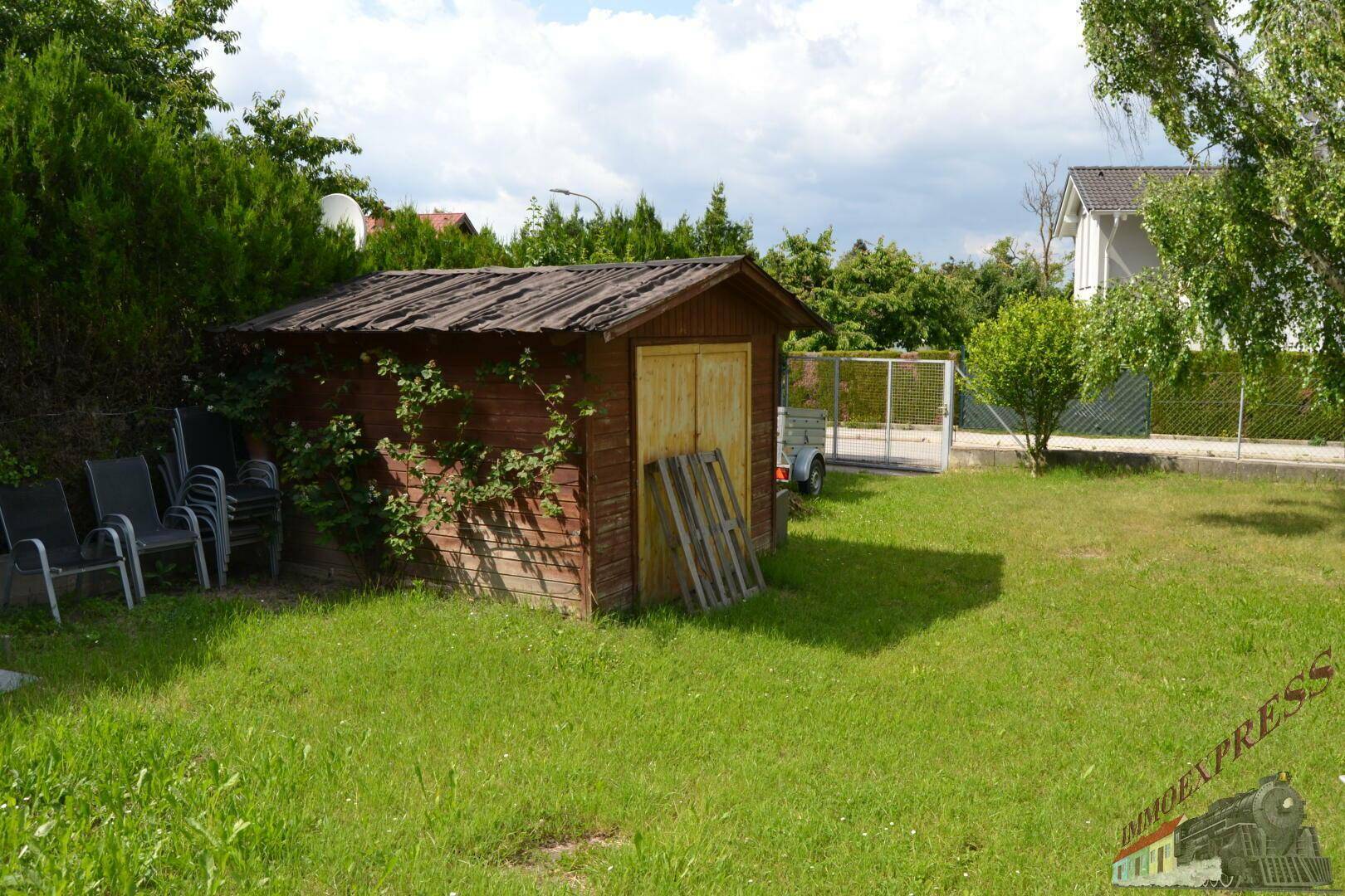 Rustikaler Holzschuppen im Garten mit Rankpflanzen und Gartenmöbeln im Hintergrund.