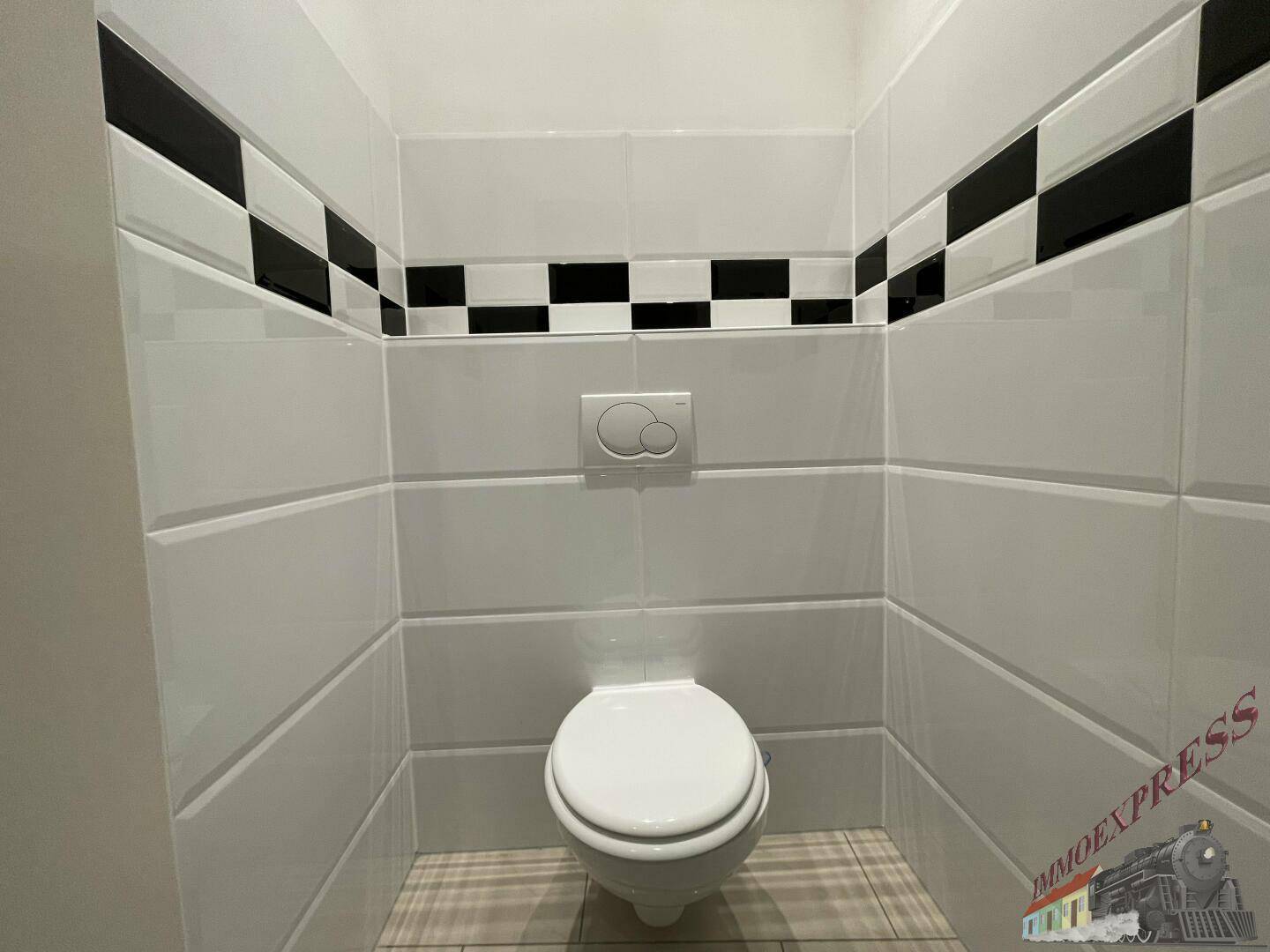 Separate Toilette mit Wand-WC und schwarz-weißem Fliesenmuster.