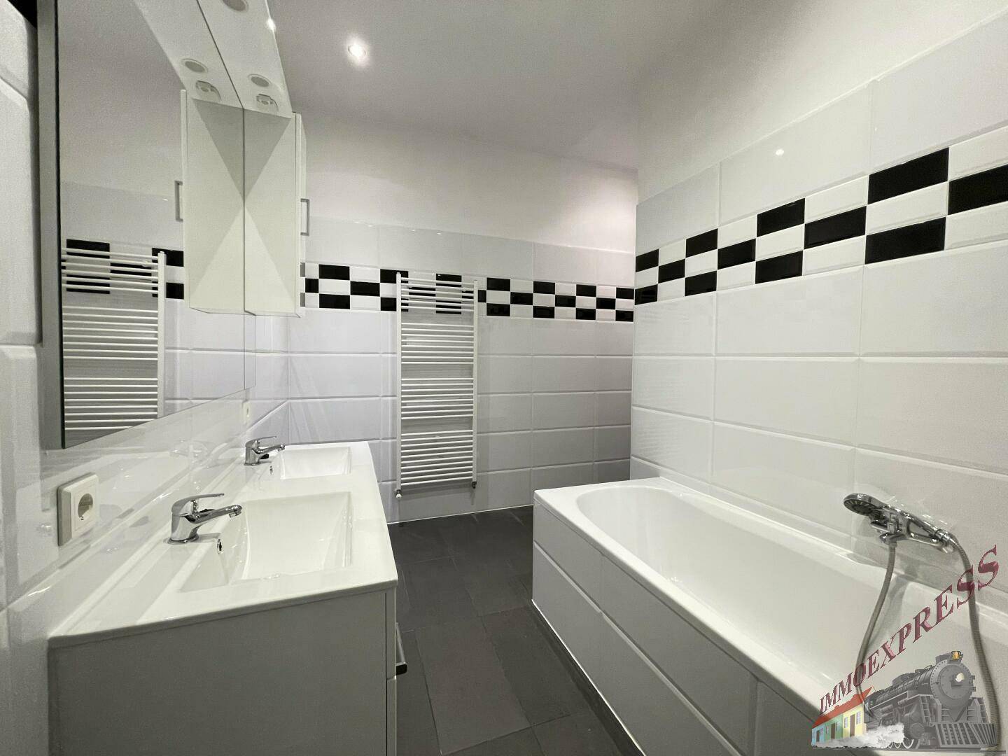 Modernes Badezimmer mit Badewanne, Doppelwaschbecken und markantem schwarz-weißem Fliesenmuster.