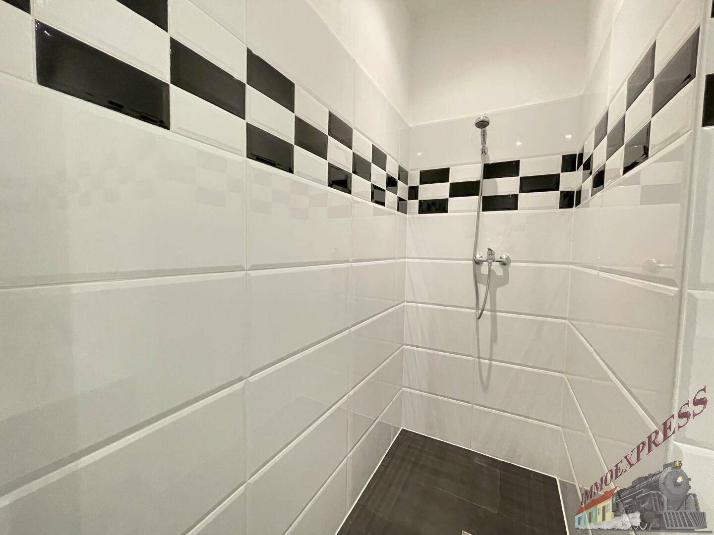 Duschbereich im Badezimmer mit modernem Fliesenmuster und Handbrause.