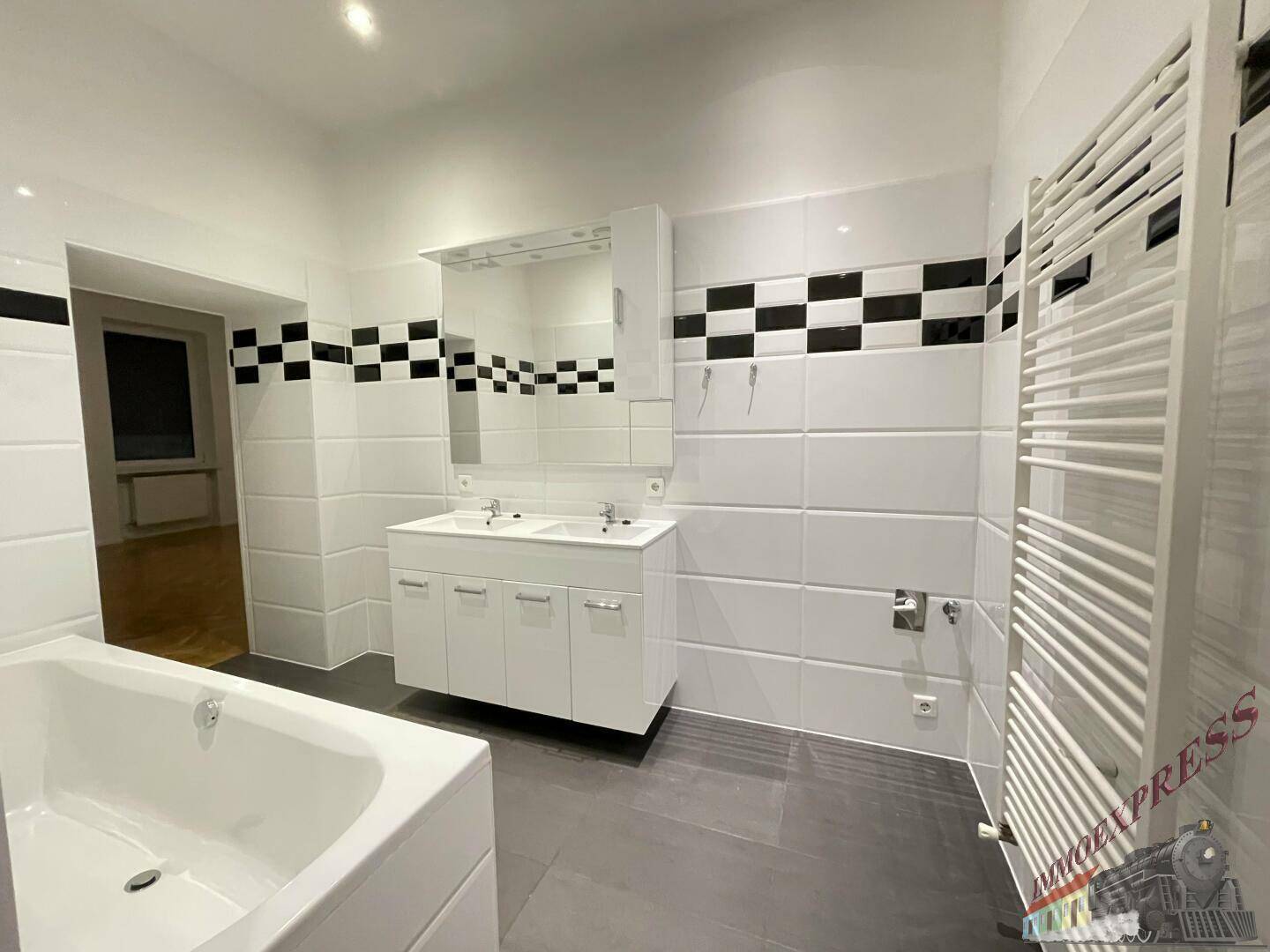 Geräumiges Badezimmer mit Badewanne, Doppelwaschbecken und Handtuchheizkörper.